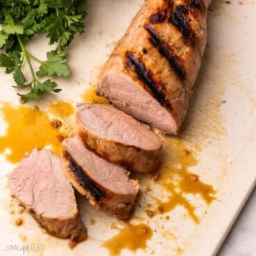 slices of pork tenderloin on a cutting board with parsley behind it.
